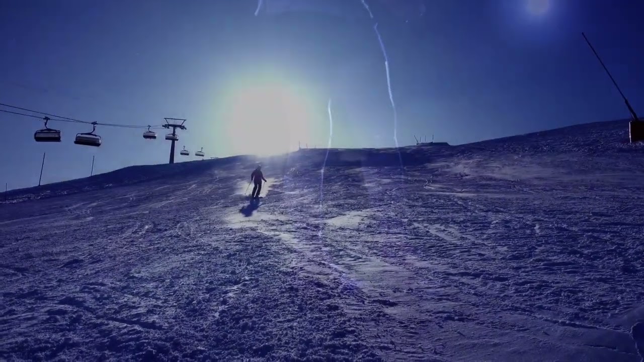A frame from the showreel: a skier silhouetted against the sun on a snowy slope, a chairlift running alongside