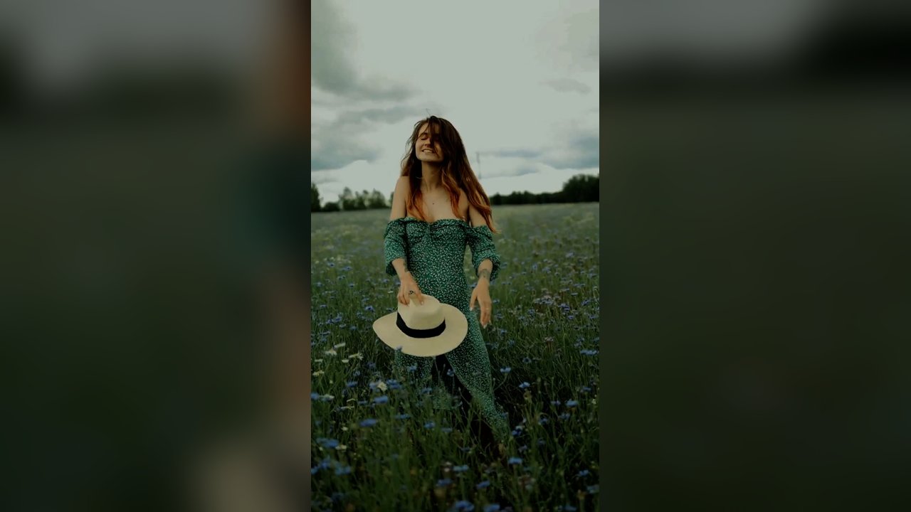 A frame from the showreel: a woman in a green dress holding a sun hat in a field of wildflowers